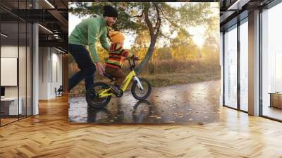 Father teaches his little child to ride bicycle in autumn park. Happy family moments. Time together dad and son. Candid lifestyle photo. Wall mural