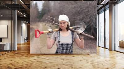 Gardener/farmer woman with spade and pitchfork on her shoulders. Tired after work. Wall mural