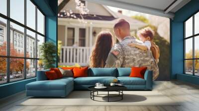 A male veteran american soldier in military uniform hugs his wife and little daughter while standing in front of their house. The concept of a emotional military happy homecoming. Sunny day Wall mural