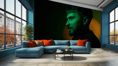 Side view artistic creative portrait of man looking away in orange neon lights on dark green background. Modern photo handsome bearded middle age man with earring in the ear. Copy space. Banner Wall mural