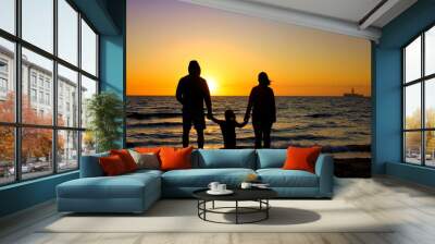 A silhouette of a young family looking out to sea in the sunset or sunrise. Wall mural