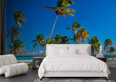 A line of exotic palm trees on a Caribbean beach showing white sand and deep blue sky with azure sea.  Wall mural