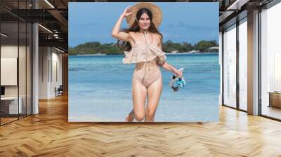 Young happy woman with wet skin, hat and snorkel walking on sand beach  Wall mural