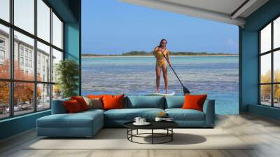 Yyoung Hispanic woman practising paddle board or sup in tropical Caribbean  turquise crystal clear calm waters in Los Roques Venezuela Wall mural