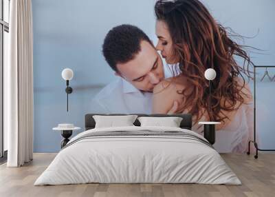 attractive newlyweds on the sea shore. Goom kissing bride's shoulder. side and back view Wall mural