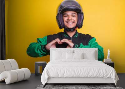 Asian online taxi driver wearing green jacket and helmet showing heart sign over yellow background Wall mural