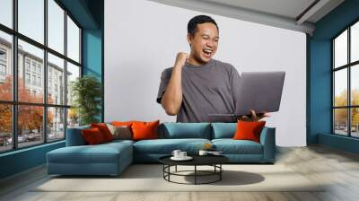 Excited Asian man with winning gesture looking to a laptop Wall mural