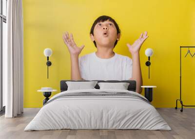 Little boy with shocked expression looking up while opening his palms isolated on yellow background Wall mural