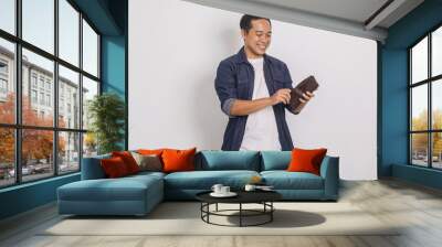 Portrait of cheerful handsome asian man looking inside his wallet isolated on white background  Wall mural