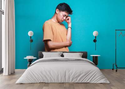 Young Asian man looking sleepy and bored over blue background Wall mural