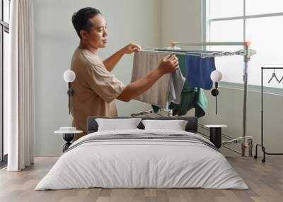 Young man does work at home, hangs clothes on clothesline. Wall mural