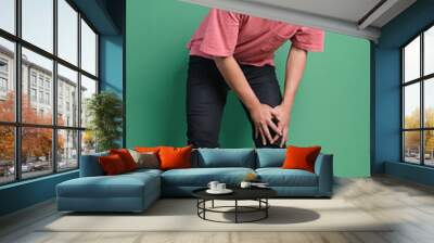 Young man suffering from knee pain over green background Wall mural