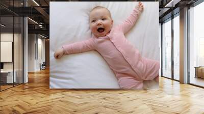 Beautiful smiling baby girl on a white bed in a pink onesie Wall mural