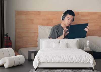 Asian handicapped teenager boy using computer and listening music video in the morning on bed and wheelchair in room, Lifestyle activities of disabled child using technology and remote learning. Wall mural