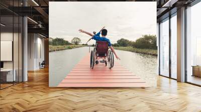 Behind of young man with disability  and father relaxing on wooden bridge jutting into the lake at the outdoor vacation in summer, People leisure travel and mental healthy concept. Wall mural