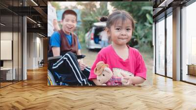 Cute Asian girl holds a teddy bear doll, Asian special child on wheelchair blurry background. Wall mural