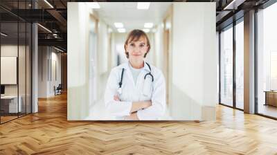 Portrait of caucasian senior woman doctor posing with arms crossed with stethoscope in hospital Wall mural