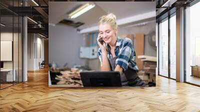 Young carpenter women using mobile phone and working in wood workshop Wall mural