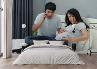 pregnant woman has a stomach ache while her husband talking a mobile phone for help on bed Wall mural