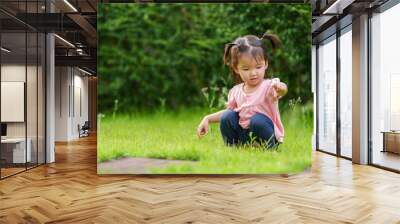 toddler girl sitting and playing grass flower in field Wall mural