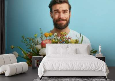 A smiling bearded man holds a vivid and diverse bouquet of flowers against a blue background, displaying a joyful and content expression in this bright portrait. Wall mural