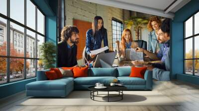 Diverse group of businesspeople discussing charts during meeting in modern office Wall mural