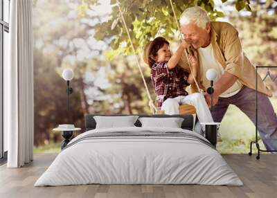 Grandfather pushing his grandson on the swing in a outdoor park Wall mural