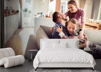 Happy young caucasian family being playful and having fun on the couch at home Wall mural