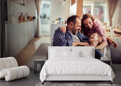 Happy young caucasian family being playful and having fun on the couch at home Wall mural