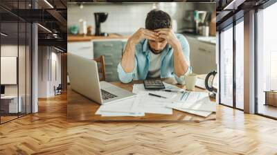 Stressed young man managing debt in kitchen Wall mural