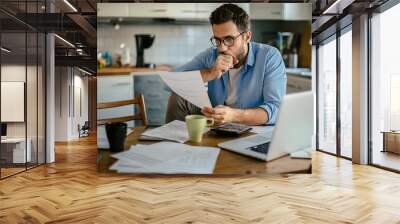 Worried young Caucasian man going over his bills and home finances in the morning in the kitchen Wall mural