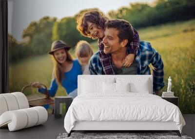 Young caucasian family having a picnic on a grassy field in nature Wall mural