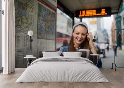 Young caucasian woman using a smart phone while waiting for a bus at the bus stop in London UK Wall mural