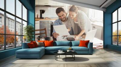 Young happy couple going over their bills at home Wall mural