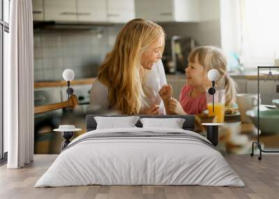 Young mother embracing her daughter while having breakfast together in the kitchen at home Wall mural