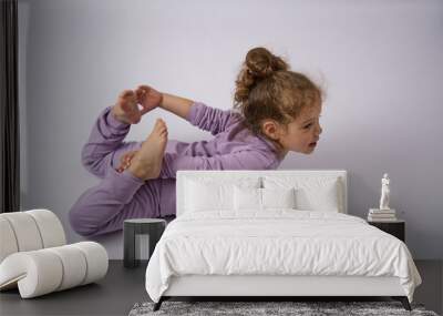 Cute little girl stretching on the floor, white background Wall mural