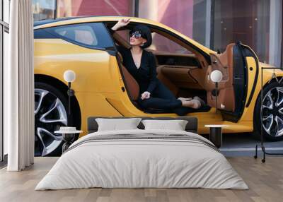 Happy beautiful young woman sitting in a yellow sports car on beautiful sunny summer day. Business Woman lady in black suit and sunglasses sitting in luxury supercar Wall mural