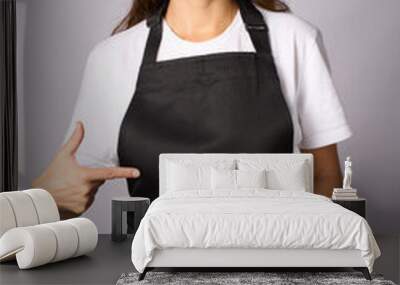 Young woman wearing black apron pointing on apron with finger Wall mural