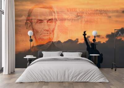 Statue of Liberty in silhouette with a portion of a warm-toned five-dollar bill in the horizon blending in with the sunrise Wall mural