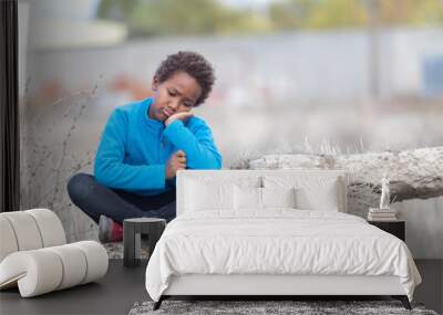 Bored child sitting on a rock in the countryside Wall mural