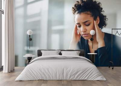 30 year old black woman with curly hair holding their head in their hands with a concerned expression, in a bright indoor business environment Wall mural