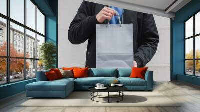 Person holding a grey shopping bag against a white wall. Wall mural