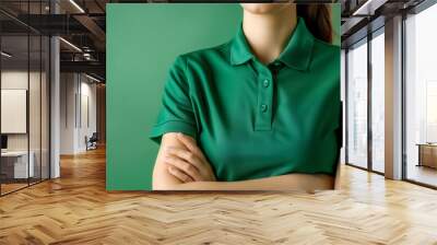 Woman in green polo shirt with arms crossed, standing against a green background. Emphasizing confidence and professionalism. high quality Wall mural