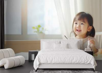 Asian cute little girl holding fork and trying to eat food sitting on the white high chair in the morning at home with copy space. : Generative AI Wall mural