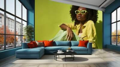 Fashion style and clothes with a model black woman sitting on the floor against a green background Portrait glasses and fashionable with a young female posing to promote trendy or edgy : Generative AI Wall mural