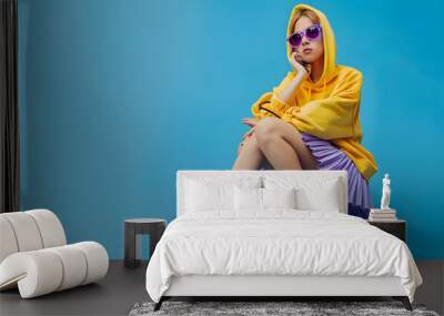 Fashionable confident girl wearing purple sunglasses pleated mini skirt yellow hoodie socks high top colorful sneakers sitting posing on blue background Fulllength studio portrait Copy : Generative AI Wall mural