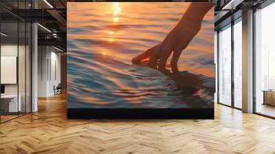 Female hand touching the calm ocean lake water surface reflecting a beautiful colorful summer sunset : Generative AI Wall mural