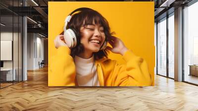 Generative AI : Happy chill asian girl listening to music in wireless headphone with smartphone Woman listening podcast and wearing yellow shirt on pink isolated background Wall mural