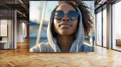 Horizontal shot of relaxed African American girl wears sunglasses and hoodie enjoys yachting and sailing poses at sea port strolls during daytime has luxury travel People leisure and l : Generative AI Wall mural