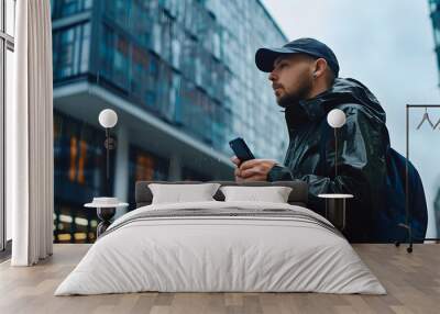 Stylish man in rainy day with smartphone stands on city street with modern building on background Wroclaw Poland : Generative AI Wall mural